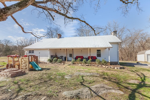 view of front of property with a chimney, metal roof, covered porch, a playground, and a front yard