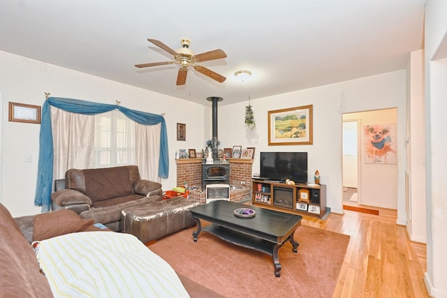 living room with ceiling fan, a wood stove, and light hardwood / wood-style floors