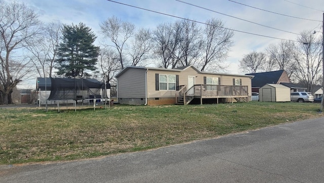 view of front of house featuring a trampoline, a wooden deck, a front yard, and a shed