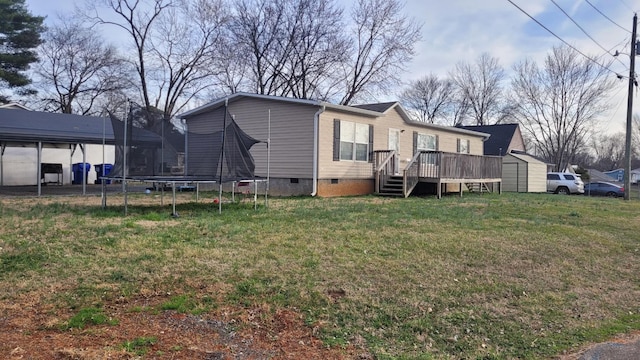 back of property with a deck, a lawn, a trampoline, and a storage unit