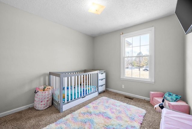 carpeted bedroom with a crib and a textured ceiling