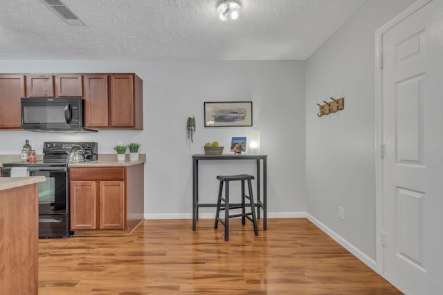 kitchen featuring a textured ceiling, light hardwood / wood-style floors, and black appliances