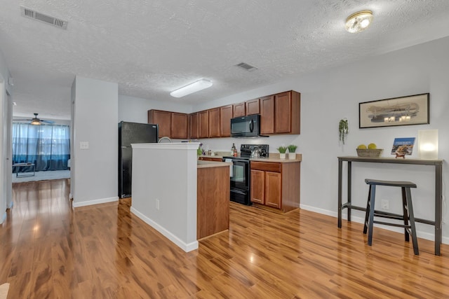 kitchen with an island with sink, a textured ceiling, light wood-type flooring, and black appliances