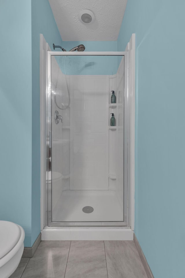 bathroom featuring toilet, a shower with shower door, tile patterned flooring, and a textured ceiling