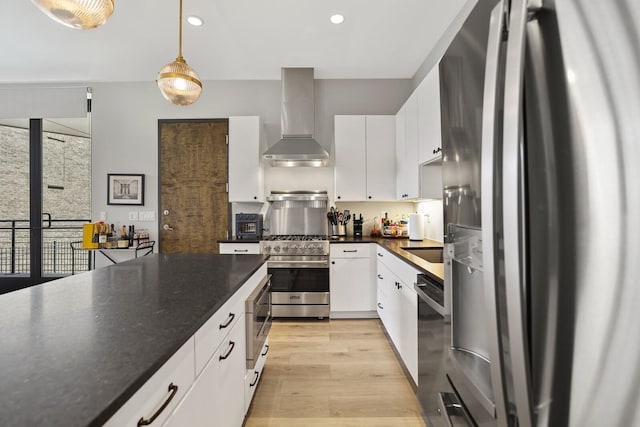 kitchen with hanging light fixtures, light wood-type flooring, appliances with stainless steel finishes, wall chimney range hood, and white cabinets