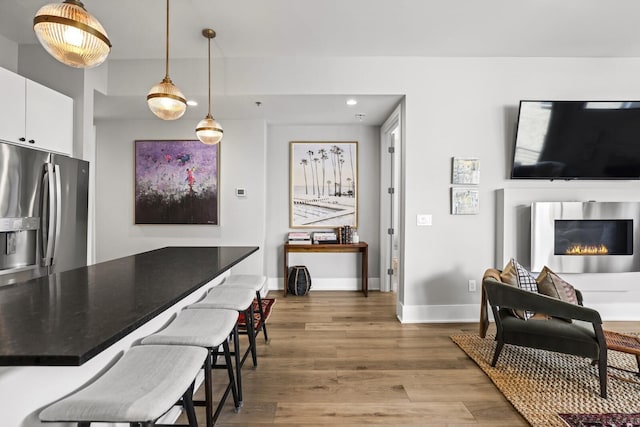 kitchen with pendant lighting, white cabinetry, a kitchen breakfast bar, hardwood / wood-style flooring, and stainless steel refrigerator with ice dispenser