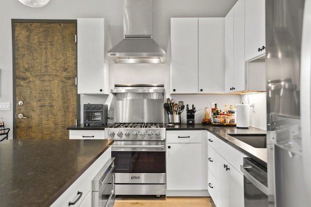 kitchen with dark stone countertops, appliances with stainless steel finishes, wall chimney range hood, and white cabinets