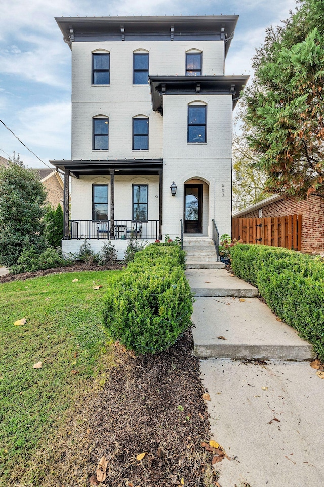 view of front of home featuring a porch, brick siding, fence, and a front lawn