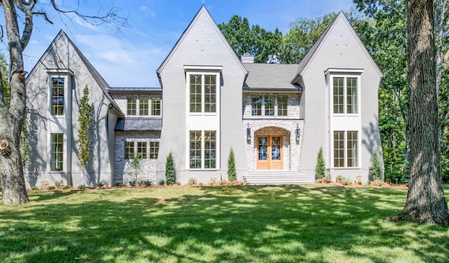 back of house featuring stone siding, french doors, a lawn, and a chimney