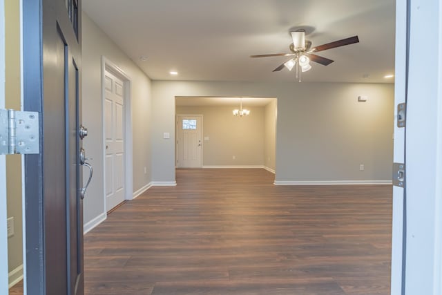 empty room with ceiling fan with notable chandelier and dark wood-type flooring