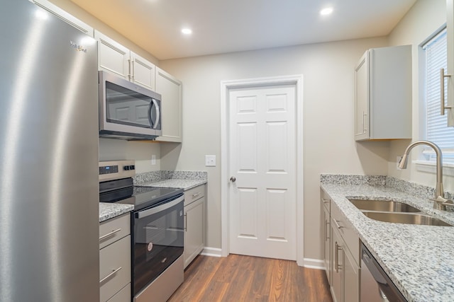 kitchen with light stone countertops, appliances with stainless steel finishes, sink, and dark wood-type flooring