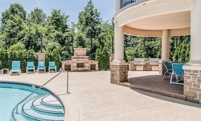 view of swimming pool featuring an outdoor kitchen, grilling area, a patio, and an outdoor stone fireplace