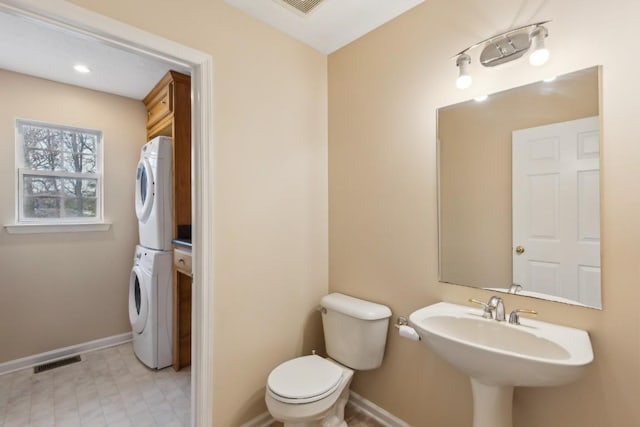 bathroom with stacked washer / drying machine, sink, and toilet