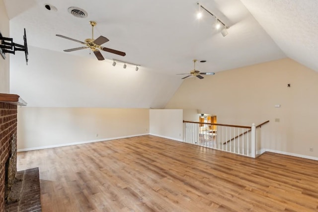 additional living space with ceiling fan, lofted ceiling, light hardwood / wood-style floors, and a brick fireplace