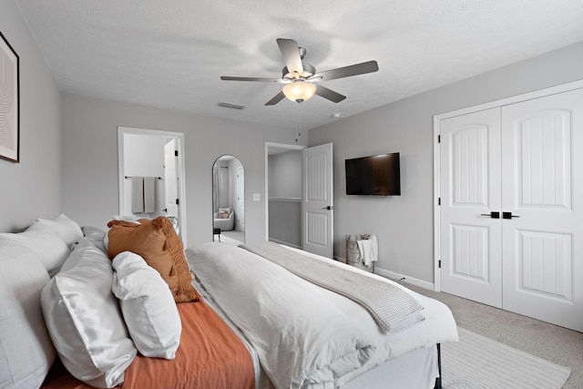 bedroom featuring ensuite bath, ceiling fan, carpet, a textured ceiling, and a closet