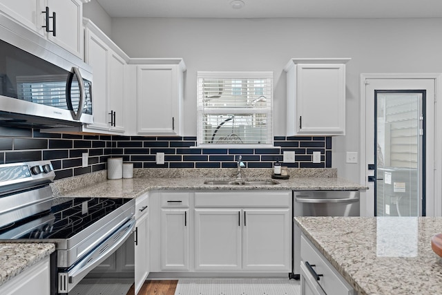 kitchen featuring appliances with stainless steel finishes, tasteful backsplash, sink, white cabinets, and light stone counters