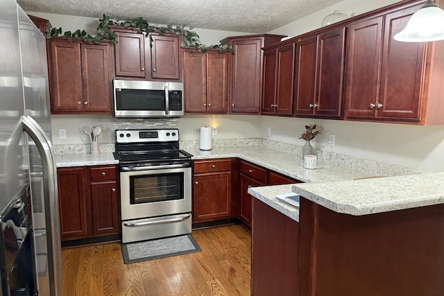 kitchen with pendant lighting, wood-type flooring, stainless steel appliances, and a textured ceiling