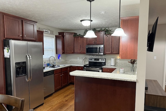 kitchen featuring appliances with stainless steel finishes, pendant lighting, sink, light hardwood / wood-style floors, and a textured ceiling