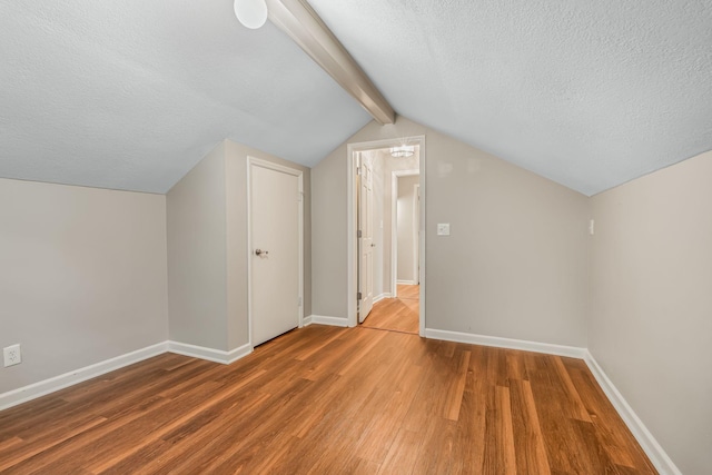 bonus room with wood-type flooring, a textured ceiling, and vaulted ceiling with beams