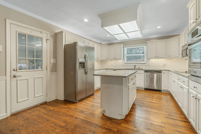 kitchen with a kitchen island, hardwood / wood-style floors, white cabinetry, light stone counters, and stainless steel appliances