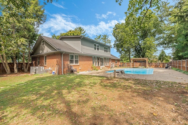 back of property with a swimming pool with hot tub, a patio, and a lawn