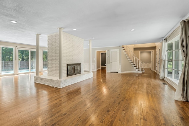 unfurnished living room with decorative columns, a brick fireplace, and hardwood / wood-style floors