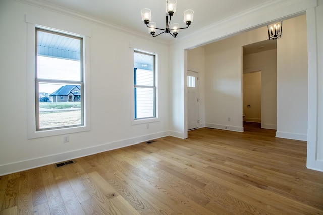 empty room featuring crown molding, a chandelier, light wood-style floors, baseboards, and visible vents