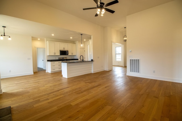 unfurnished living room with baseboards, light wood finished floors, visible vents, and ceiling fan with notable chandelier