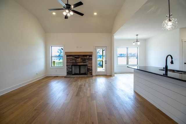 unfurnished living room with vaulted ceiling, wood finished floors, a ceiling fan, a sink, and a fireplace