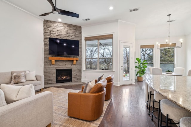 living room featuring crown molding, a stone fireplace, a wealth of natural light, and ceiling fan with notable chandelier