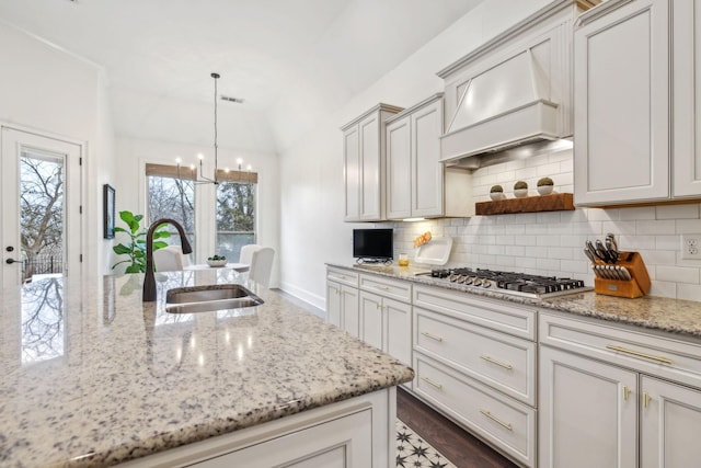 kitchen with pendant lighting, sink, light stone counters, tasteful backsplash, and stainless steel gas stovetop