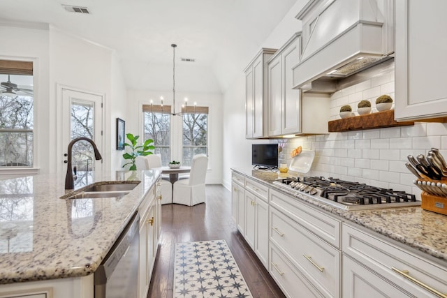 kitchen with sink, premium range hood, appliances with stainless steel finishes, hanging light fixtures, and light stone countertops