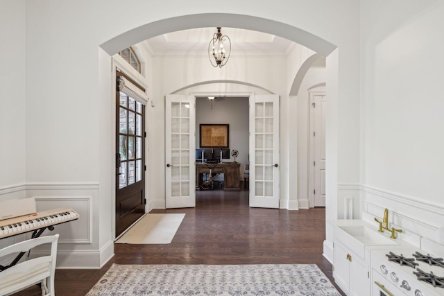 entryway with an inviting chandelier, dark wood-type flooring, ornamental molding, and french doors