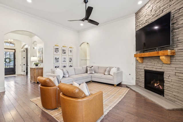 living room with crown molding, ceiling fan, a stone fireplace, and hardwood / wood-style floors