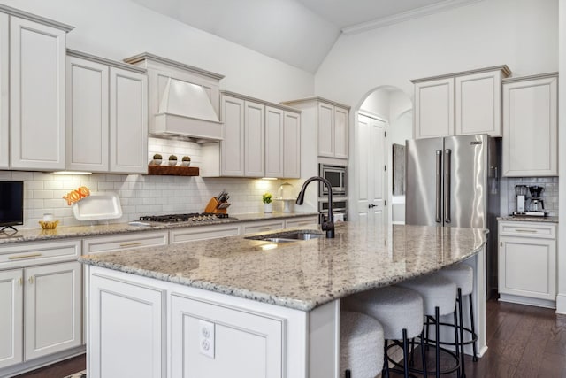 kitchen with sink, appliances with stainless steel finishes, an island with sink, decorative backsplash, and custom exhaust hood