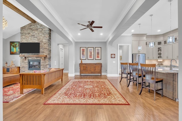 living room featuring sink, light wood-type flooring, ornamental molding, ceiling fan, and a fireplace