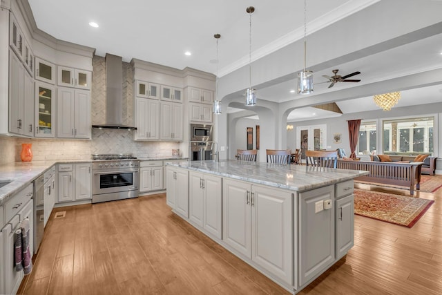 kitchen featuring wall chimney exhaust hood, decorative light fixtures, a center island, appliances with stainless steel finishes, and light stone countertops