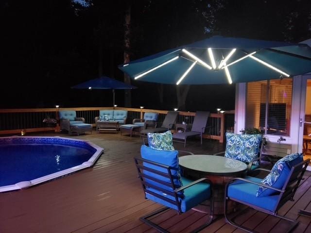 pool at night featuring outdoor lounge area and a deck