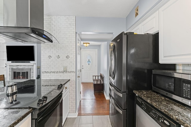 kitchen with appliances with stainless steel finishes, white cabinetry, backsplash, dark stone countertops, and range hood