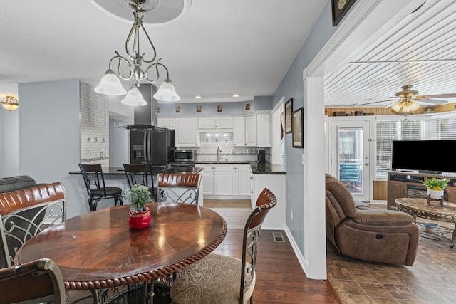 dining area with wood-type flooring, sink, and ceiling fan with notable chandelier