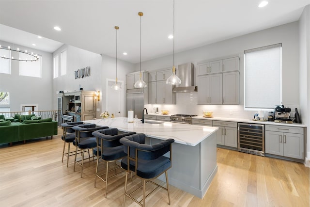 kitchen featuring gray cabinetry, premium appliances, decorative light fixtures, beverage cooler, and wall chimney exhaust hood