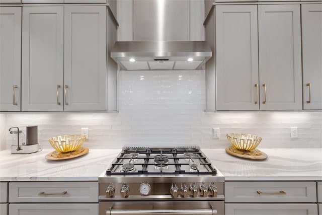 kitchen featuring light stone counters, stainless steel gas range, wall chimney exhaust hood, and gray cabinets