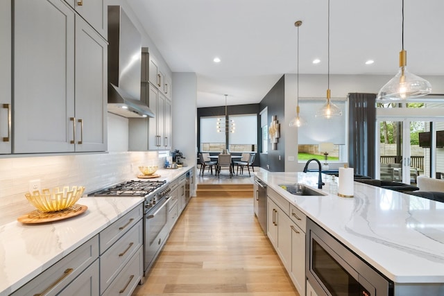 kitchen with light stone counters, hanging light fixtures, stainless steel appliances, and wall chimney exhaust hood