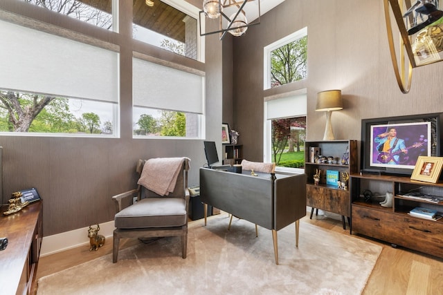 living area with an inviting chandelier, plenty of natural light, wood-type flooring, and a high ceiling