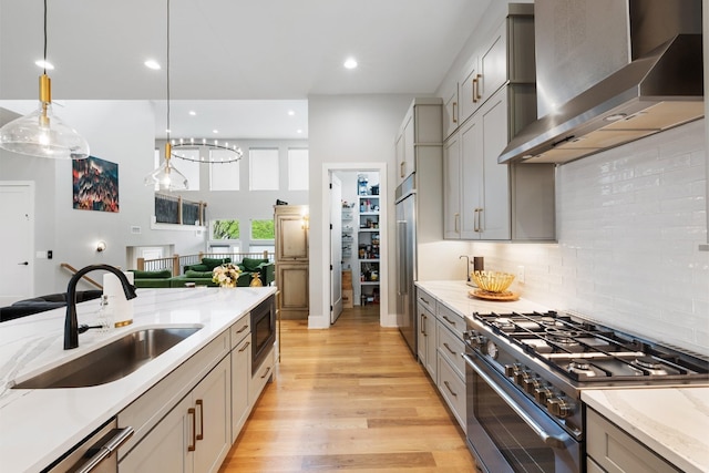 kitchen featuring wall chimney exhaust hood, sink, high end appliances, decorative light fixtures, and gray cabinets