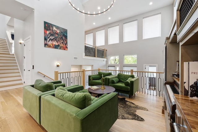 living room with a notable chandelier, a towering ceiling, and light wood-type flooring