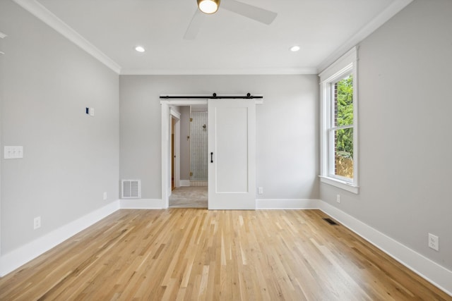 spare room featuring crown molding, light hardwood / wood-style flooring, a barn door, and ceiling fan