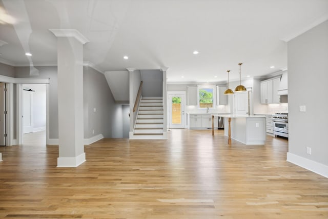 unfurnished living room with ornate columns, ornamental molding, and light wood-type flooring