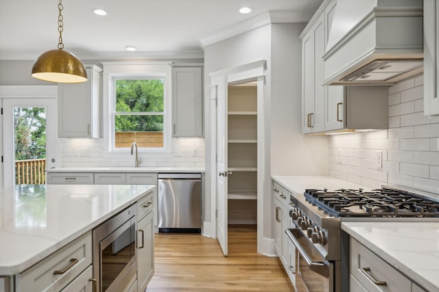 kitchen featuring pendant lighting, appliances with stainless steel finishes, light stone counters, light hardwood / wood-style floors, and custom range hood