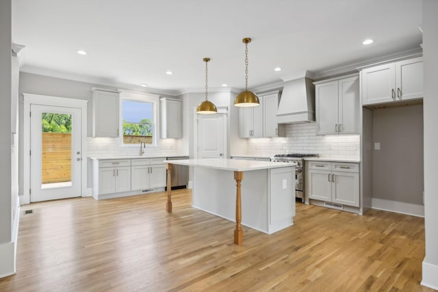 kitchen with sink, hanging light fixtures, appliances with stainless steel finishes, a kitchen island, and custom range hood